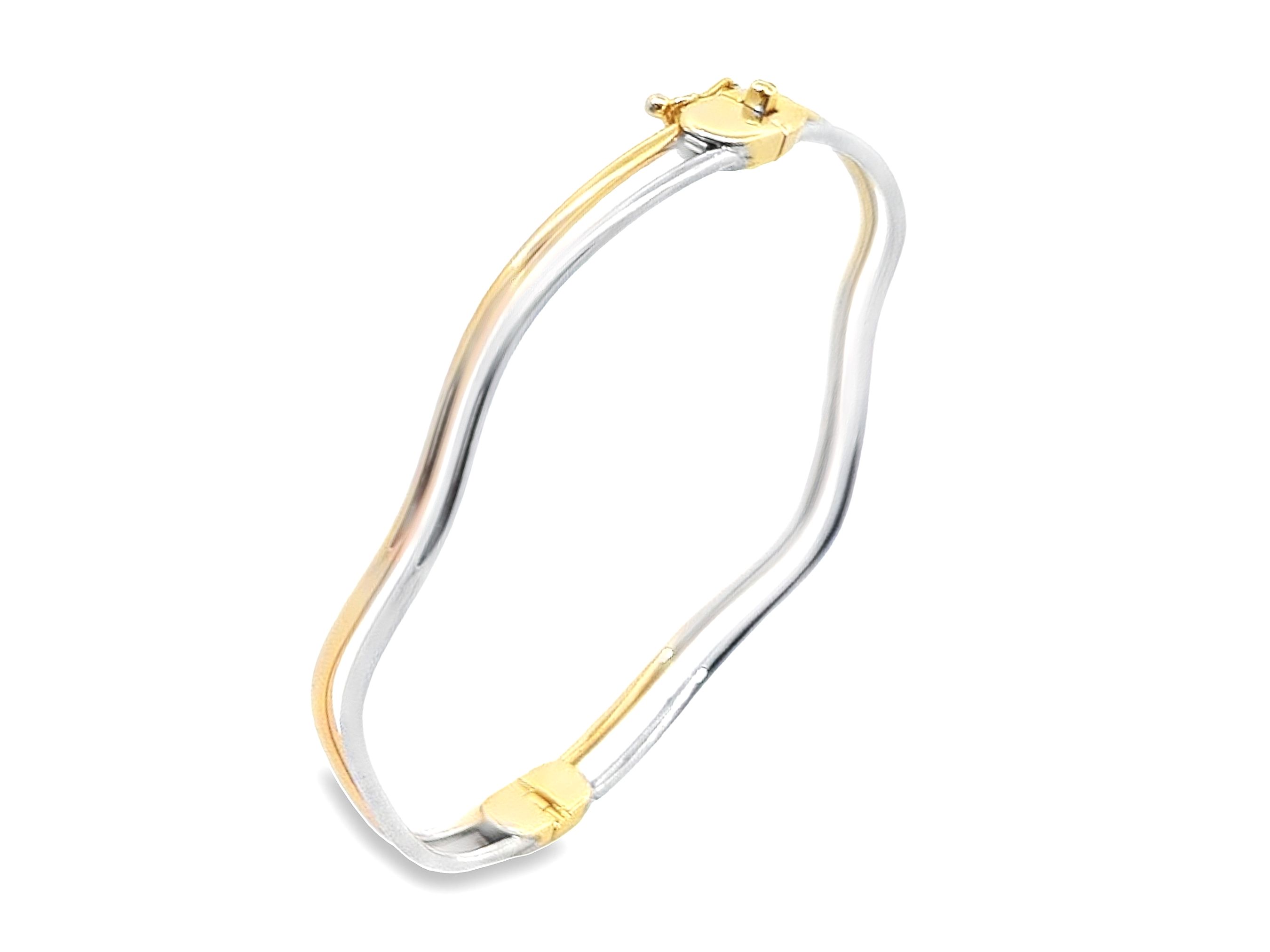 Deze bangle van Louis Bros is vervaardigd uit 14 karaat bicolor (8.gr.). De armband heeft een dikte van 1.60 mm en een breedte van 5 mm. 
Deze bangle met een bijzondere vorm is een opvallend sieraad dat stijl en originaliteit combineert. De combinatie van wit- en geelgoud geeft deze bangle een unieke en moderne uitstraling. Door het gebruik van twee kleuren goud ontstaat er een prachtig contrast, waardoor de bijzondere vorm van de armband nog beter tot zijn recht komt. Deze bangle is niet alleen een elegante toevoeging aan elke sieradencollectie, maar ook een statement piece dat elke outfit naar een hoger niveau tilt. Het innovatieve ontwerp en de hoogwaardige materialen maken deze bangle tot een tijdloos en verfijnd sieraad dat zowel klassiek als eigentijds is.