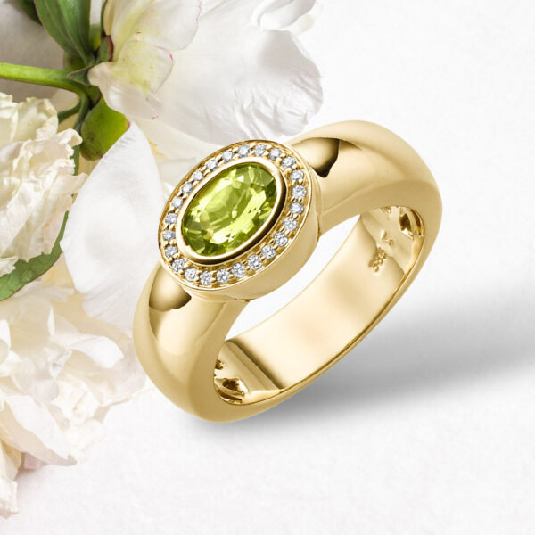 De Brede ring met modelnummer GBG0050, is gemaakt van 14-karaats geelgoud en bevat een ovale peridot van 0.78 Crt omgeven door een Halo van diamant. Draag deze elegante ring voor speciale gelegenheden of als een opvallend accessoire bij dagelijkse outfits voor extra groene flair.