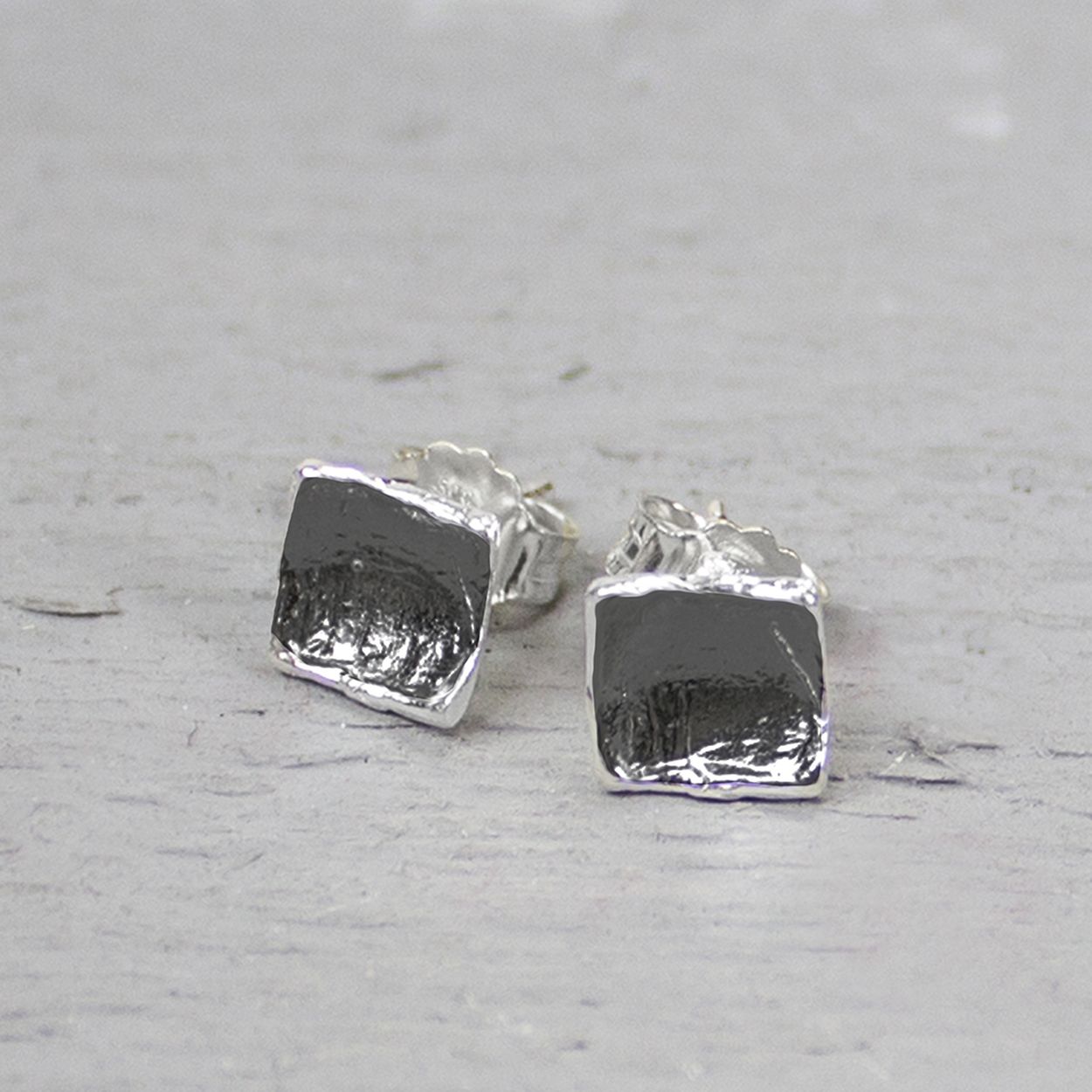 De oorknopjes gemaakt van 925 sterling zilver en geoxideerd zilver hebben een vierkante vorm. Doordat de vierkantjes gebogen zijn wordt er een driedimensionaal effect gecreëerd.