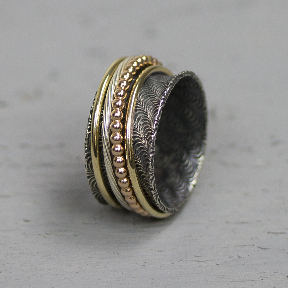 Ring gemaakt van 925 geoxideerd sterling zilver met draaiende ringen van rose en geel goldfilled. In de bais ring zit een golvende structuur. De glans van 925 sterling zilver maakt het een gewild edelmetaal voor de vervaardiging van sieraden. Het bestaat uit 92,5% puur zilver en 7,5% koper. Puur zilver is een zacht en buigzaam materiaal, het koper in 925 sterling zilver zorgt voor de stevigheid. De sieraden van Jeh Jewels zijn nikkel vrij. Op dit sieraad is gebruik gemaakt van geoxideerd zilver, dit is een oppervlakte bewerking. Het is mogelijk dat de geoxideerde laag na verloop van tijd door slijtage vervaagd. Goldfilled komt uit Amerika en wordt daar al langer gebruikt voor de vervaardiging van sieraden met een "touch of gold" voor een betaalbare prijs. Het goldfilled blijft op kleur, is slijtvast en de goudlaag is dik genoeg om lang te kunnen genieten van de warme uitstraling van goud. Goldfilled wordt veelal ook goed verdragen door mensen die allergisch zijn voor andere metalen dan goud.