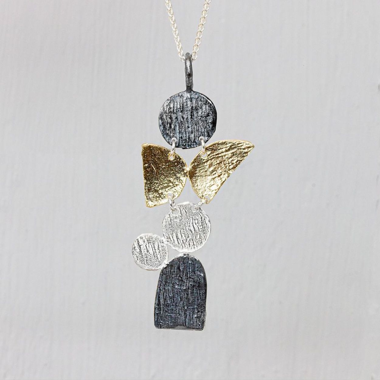 Dit collier is gemaakt van zilver met onderin een drie kleurige hanger. De combinatie van geoixideerd zilver, verguld zilver en zilver geeft de perfecte look. Het reliëf maakt dit collier helemaal af.