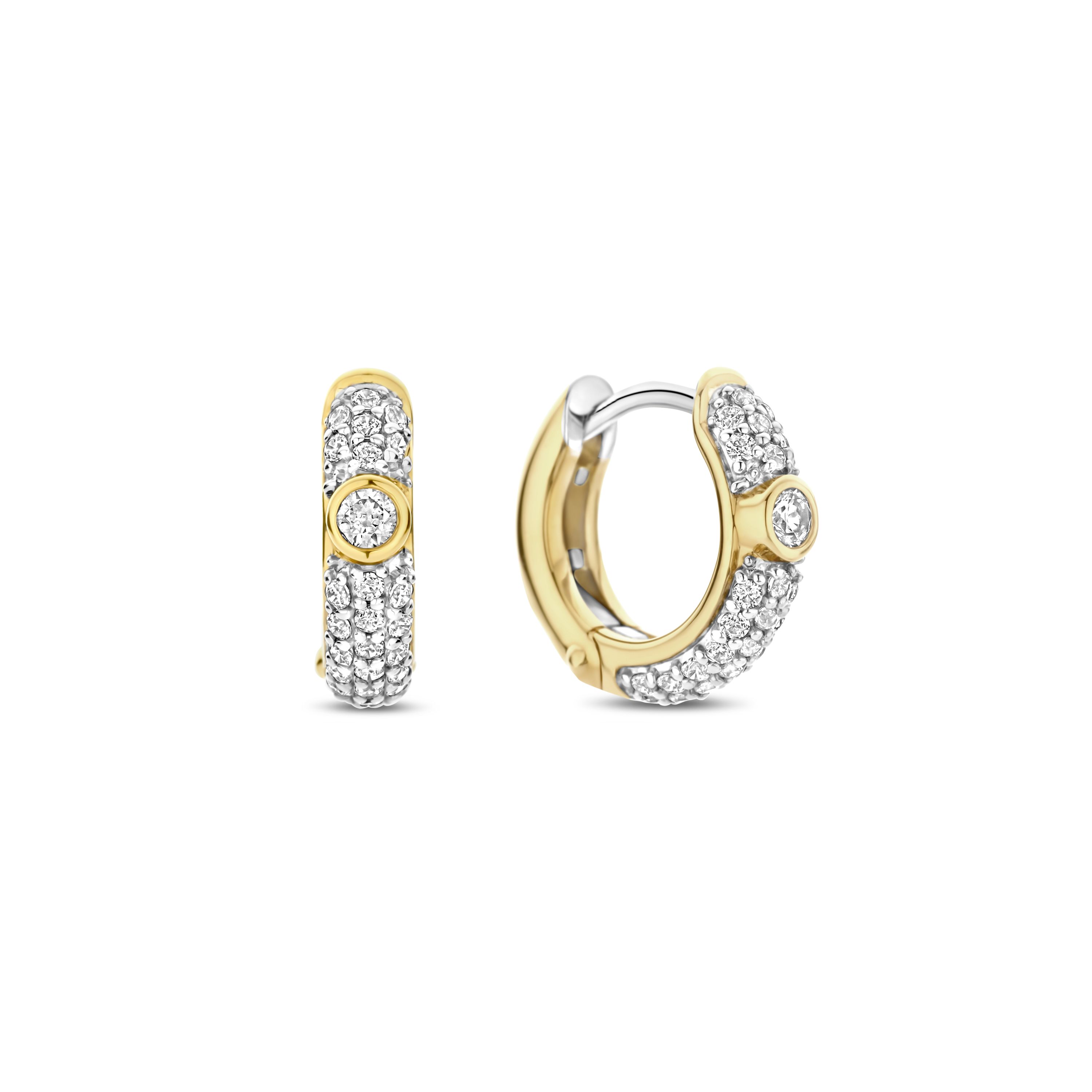Deze TI SENTO oorbellen 78019ZY zijn een sprankelende mix van moderne glamour en klassieke elegantie. Gemaakt van hoogwaardig 925 sterling zilver, zijn deze oorbellen rijkelijk versierd met pav�gezette cubic zirconia, wat een eindeloos schitterend effect cre�ert. Een bezelgezette solitaire cubic zirconia, omhuld in warme goudkleurige plating, staat centraal en voegt een opvallend contrast en vleugje schittering toe.

Ontworpen om indruk te maken, zijn deze hoepels perfect voor dag-naar-nacht styling�ze bieden precies de juiste hoeveelheid sprankeling voor een verfijnde daglook of een oogverblindende avondstatement. De veilige scharnier sluiting zorgt voor een comfortabele pasvorm, terwijl de mix van pav� en bezelgezette stenen dimensie en textuur aan dit verfijnde ontwerp toevoegt. Nikkelvrij en hypoallergeen, beloven ze luxueus comfort bij elk draagmoment. Een moderne klassieker met een gouden gloed, deze oorbellen zijn een onmisbare toevoeging aan je sieradenrepertoire.