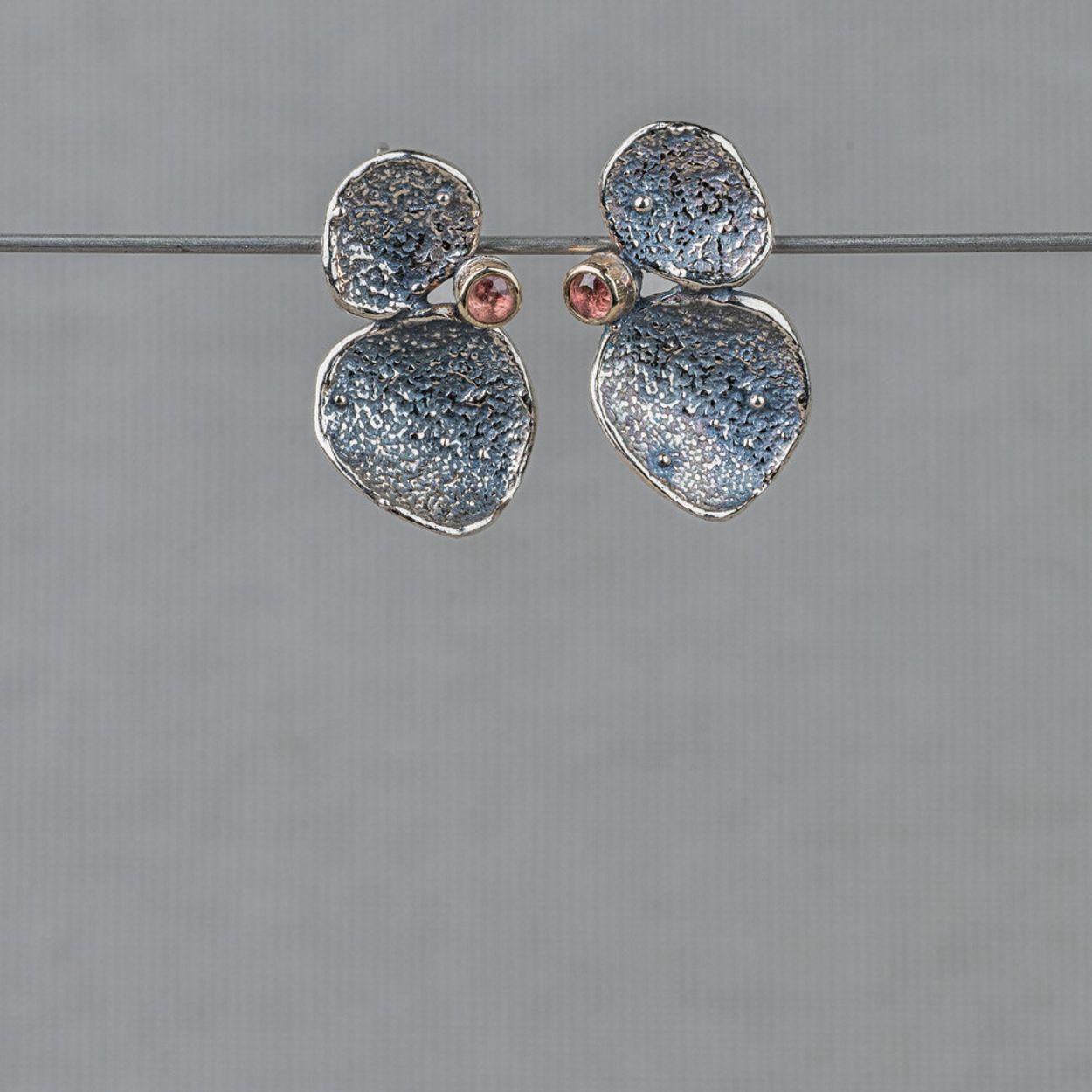 Oorstekers gemaakt van 925 sterling zilver, geoxideerd zilver en een zetting van 10 karaat met daarin een Roze Toermalijn. Toermalijn werkt aardend, beschermend en reinigend. Deze edelsteen is zeer geschikt om te gebruiken als bescherming tegen negatieve energie. Deze oorbellen kunnen perfect gecombineerd worden met de andere sieraden uit de Aztec collectie.