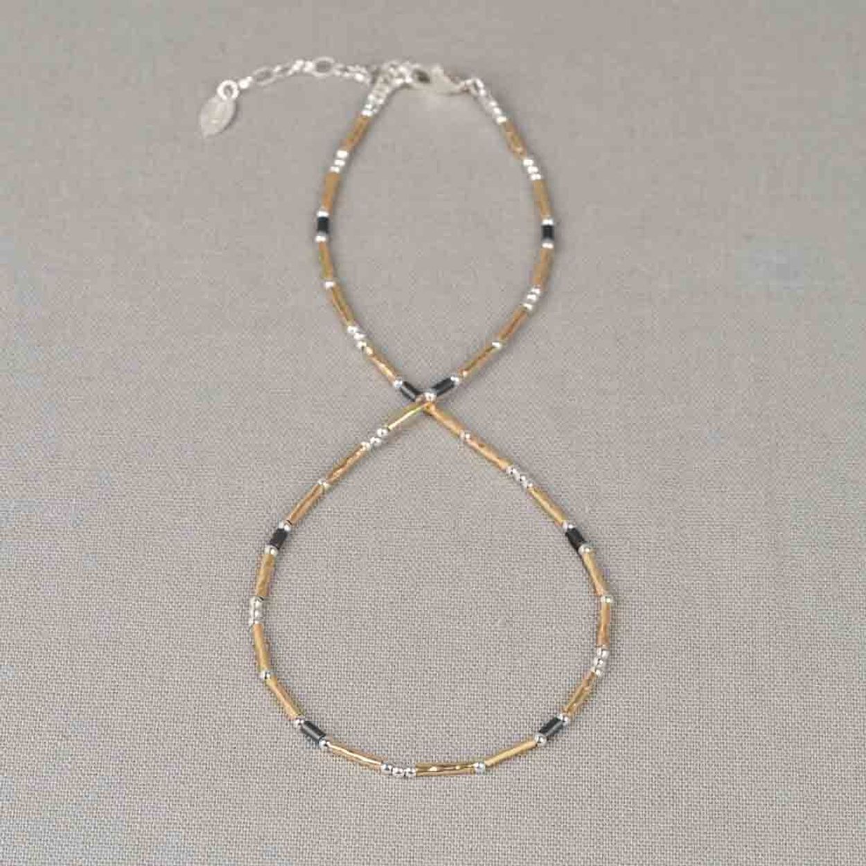 Dit verfijnde collier is opgebouwd uit 925 sterling zilveren balletjes en Goldfilled buisjes, gecombineerd met de edelsteen Hematiet. De afwisseling van ronde en langwerpige elementen zorgt voor een speels effect. De warme glans van Goldfilled vormt een mooi contrast met het koele 925 sterling zilver en de diepe, donkere tint van Hematiet. Combineer met het bijpassende armbandje voor een complete look!