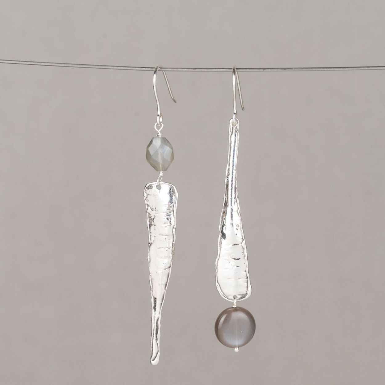Deze oorhangers zijn uitgevoerd in zilver met een oxy shiny afwerking en gecombineerd met grijze Maansteen. De langgerekte, organisch gevormde hanger heeft een stoere, ambachtelijke uitstraling, terwijl de afwerking zorgt voor een subtiel contrast tussen donker en glanzend zilver. De grijze Maansteen voegt een zachte glans toe en brengt balans in het design. De combinatie van strakke vorm en natuurlijke steen geeft deze oorhangers een eigentijdse en verfijnde uitstraling.
