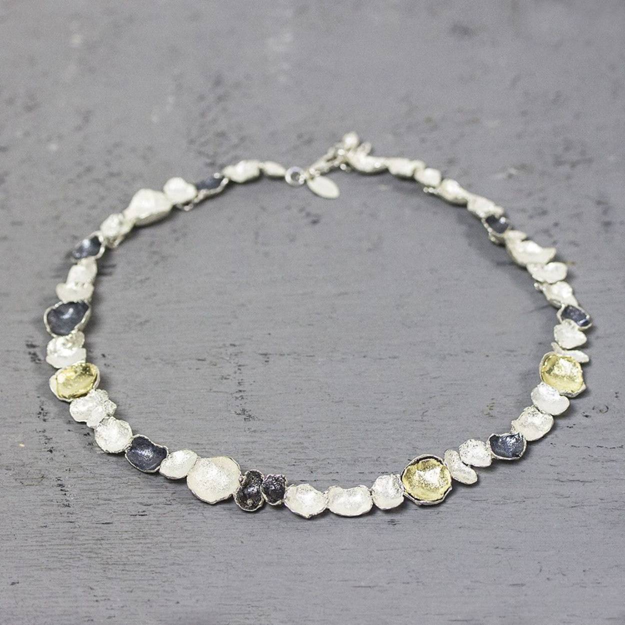 Collier gemaakt van 925 sterling zilver, geoxideerd zilver en zilver verguld. Dit schakelcollier is door de drie kleuren en verschillende organische schaaltjes een echt Jéh collier.