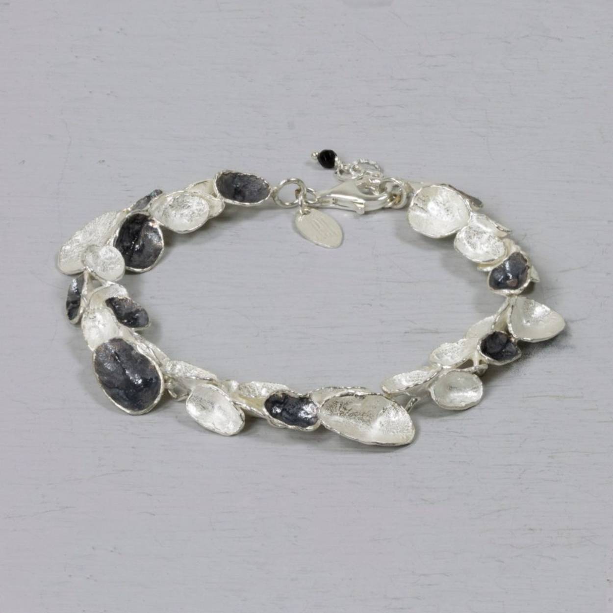 Deze armband van Jéh Jewels is gemaakt van 925 sterling wit zilver met geoxideerd zilver. Deze organische ronde armband, past door de combinatie van de twee kleuren bij verschillende colliers uit de Jéh collectie.

Materiaal: 925 sterling zilver
De glans van 925 sterling zilver maakt het een gewild edelmetaal voor de vervaardiging van sieraden. Het bestaat uit 92,5% puur zilver en 7,5% koper. Puur zilver is een zacht en buigzaam materiaal, het koper in 925 sterling zilver zorgt voor de stevigheid. De sieraden van Jéh Jewels zijn nikkel vrij.

Materiaal: Geoxideerd zilver
Op dit sieraad is gebruik gemaakt van geoxideerd zilver, dit is een oppervlakte bewerking. Het is mogelijk dat de geoxideerde laag na verloop van tijd door slijtage gaat vervagen.
