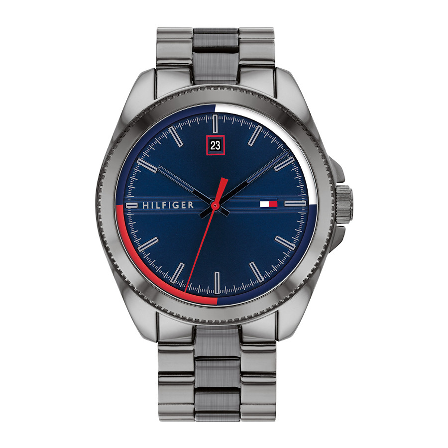 Het herenhorloge is voorzien van een grijsstalen kast met een afmeting van 44 mm met blauwe wijzerplaat waarop rood-wit-blauwe accenten, index, wijzers en het TOMMY HILFIGER logo. De grijze, stalen horlogeband met schakels sluit door middel van een vouwsluiting.