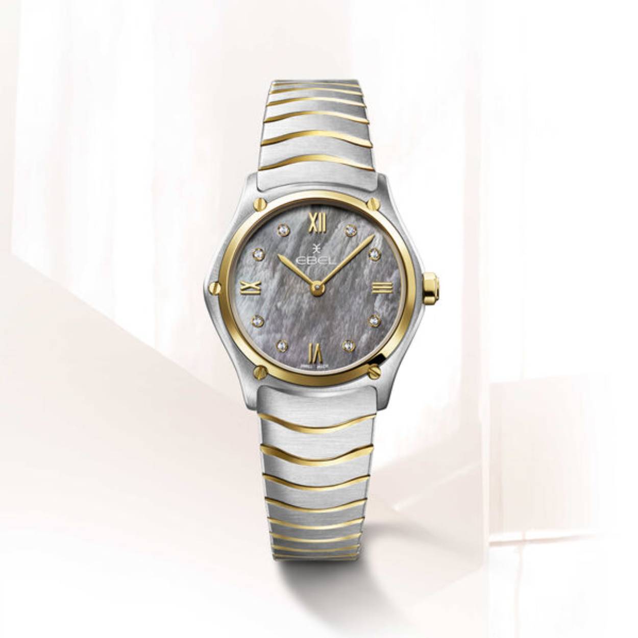 Bestel dit EBEL Sport Classic dames horloge op onze webshop. Het model met het referentienummer 1216642 is uitgerust met een Zwitsers top kwaliteit Quartz uurwerk. Het uurwerk is geplaatst in een hoogwaardige edelstalen horlogekast met een 18 kt. geelgouden bezel, schroefdetails en kroon. Op de grijze parelmoer wijzerplaat is met geelgouden PVD wijzers en Romeinse cijfers tezamen met 8 diamanten de tijd op analoge wijze af te lezen. De diamanten zijn Top Wesselton VS kwaliteit en hebben een totaalgewicht van 0.052 ct. De edelstalen geschakelde horlogeband met geelgouden PVD delen is aan de ronde horlogekast van 29 mm. gemonteerd. De band is voorzien van een vouwsluiting, met het EBEL logo. Deze sluiting zorgt ervoor dat uw horloge niet zomaar van uw pols kan glijden.