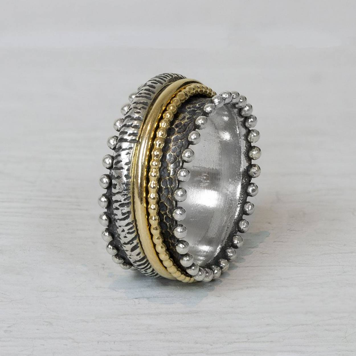 Ring van van Jéh Jewels gemaakt van geoxideerd zilver, en goldfilled. Deze lieve ring heeft, net als vele van de ringen van Jeh, goldfilled bandjes die in het midden kunnen draaien. De bolletjes aan de zijkant maken deze ring extra leuk!

Materiaal: Geoxideerd zilver
Op dit sieraad is gebruik gemaakt van geoxideerd zilver, dit is een oppervlakte bewerking. Het is mogelijk dat de geoxideerde laag na verloop van tijd door slijtage gaat vervagen.

Materiaal: Goldfilled
Goldfilled komt uit Amerika en wordt daar al langer gebruikt voor de vervaardiging van sieraden met een "touch of gold" voor een betaalbare prijs. Het goldfilled blijft op kleur, is slijtvast en de goudlaag is dik genoeg om lang te kunnen genieten van de warme uitstraling van goud. Goldfilled wordt veelal ook goed verdragen door mensen die allergisch zijn voor andere metalen dan goud.

Materiaal: 925 sterling zilver
De glans van 925 sterling zilver maakt het een gewild edelmetaal voor de vervaardiging van sieraden. Het bestaat uit 92,5% puur zilver en 7,5% koper. Puur zilver is een zacht en buigzaam materiaal, het koper in 925 sterling zilver zorgt voor de stevigheid. De sieraden van Jéh Jewels zijn nikkel vrij.