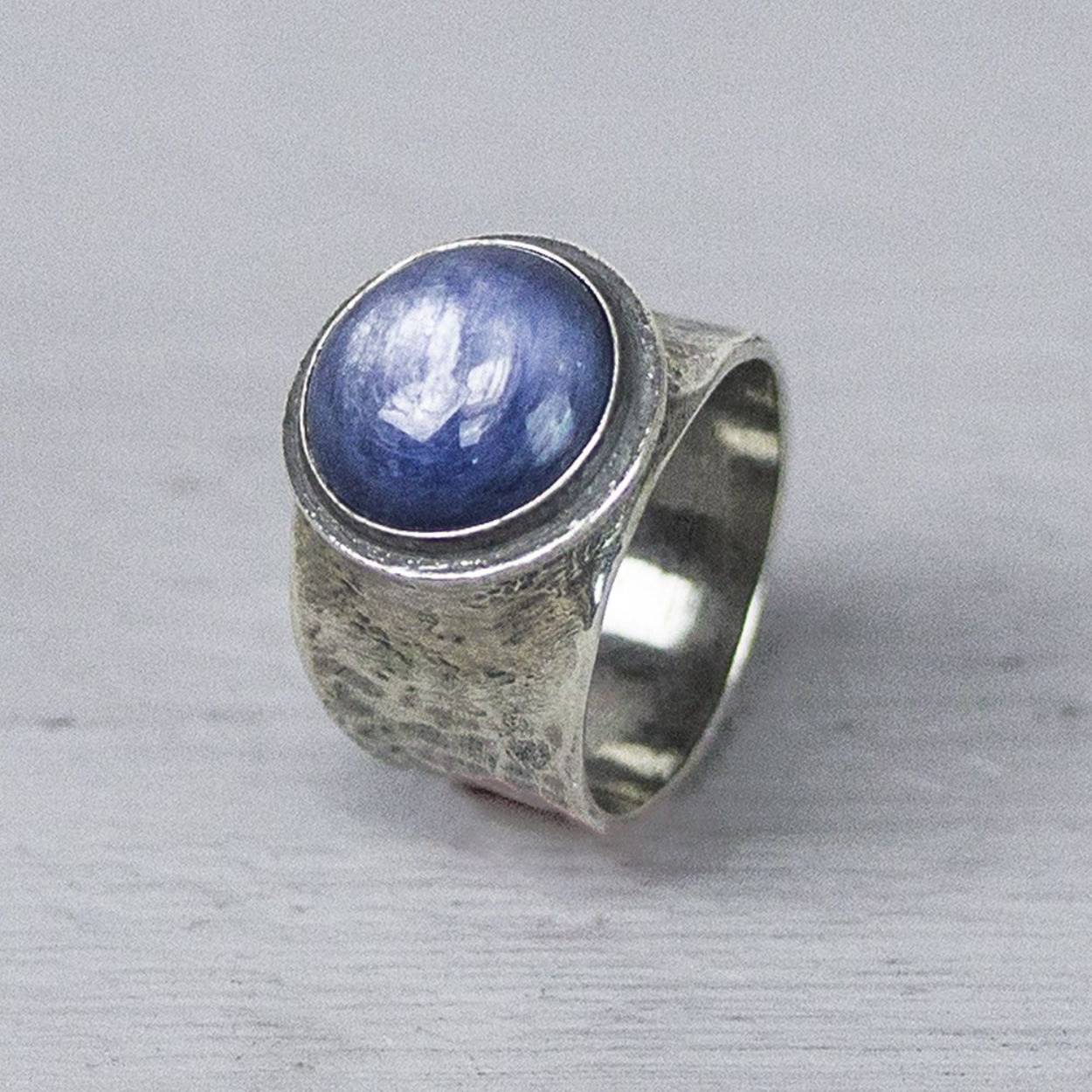 Ring gemaakt van 925 geoxideerd sterling zilver, met een edelsteen cabochon geslepen van Kyaniet. Kyaniet is een spirituele steen met een kalmerende en evenwichtige werking. Het helpt ons de regie over ons eigen leven voeren en om in te zien dat we geen marionetten van het lot zijn maar onze eigen toekomst vorm kunnen geven.