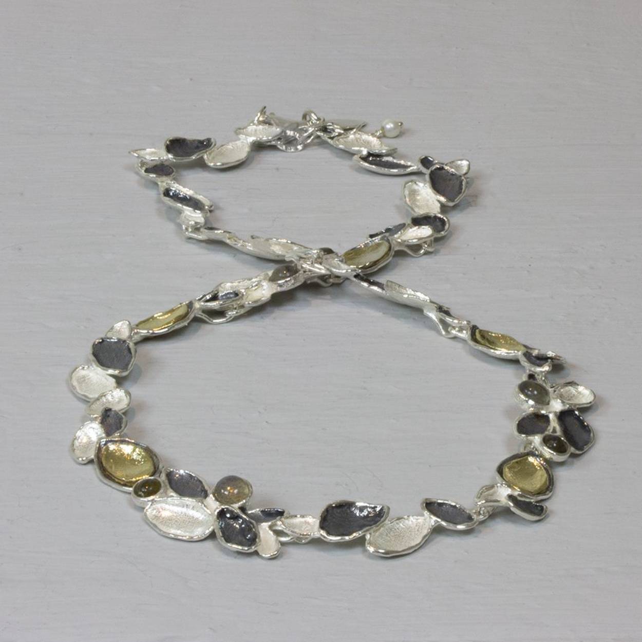 Collier gemaakt van blaadjes van 925 sterling zilver, geoxideerd zilver en zilver verguld met tussen de blaadjes Labradotiet.

Materiaal: 925 sterling zilver
De glans van 925 sterling zilver maakt het een gewild edelmetaal voor de vervaardiging van sieraden. Het bestaat uit 92,5% puur zilver en 7,5% koper. Puur zilver is een zacht en buigzaam materiaal, het koper in 925 sterling zilver zorgt voor de stevigheid. De sieraden van Jéh Jewels zijn nikkel vrij.

Materiaal: Geoxideerd zilver
Op dit sieraad is gebruik gemaakt van geoxideerd zilver, dit is een oppervlakte bewerking. Het is mogelijk dat de geoxideerde laag na verloop van tijd door slijtage gaat vervagen.

Materiaal: Zilver verguld
Vergulden is het bedekken van een voorwerp met een laagje goud. Dit artikel is door een goudbad gehaald wat ervoor zorgt dat het zilver volledig bedekt wordt met een laagje goud. Resultaat een mooie glanzende afwerking met een laagje echt goud wat ook wel silverplated of goldplated wordt genoemd.

Materiaal: Edelstenen
Bij Jéh Jewels werken wij met echte edelstenen, dit zijn natuurlijke producten waardoor niet iedere steen hetzelfde is. Ieder sieraad is hierbij dus uniek. De kleur en structuur van de steen kan afwijken van de foto op de website.