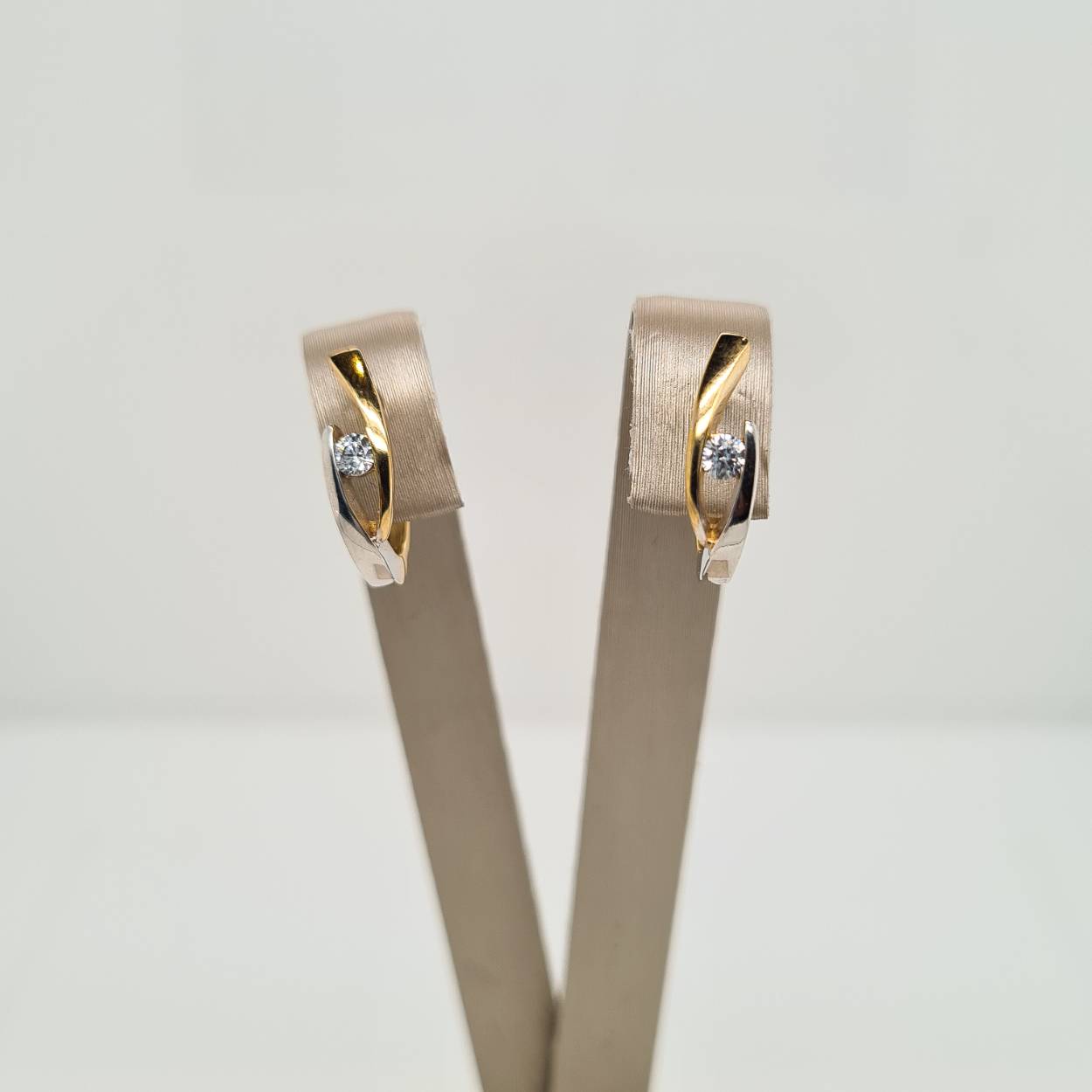 14krt geel- en witgouden klapoorringen uitgevoerd met een heldere zirkonia. De oorringen zijn bicolor gestift en hebben een afmeting van 15x4mm.